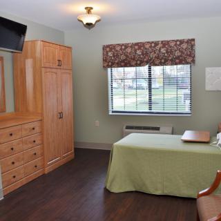 A neatly arranged bedroom with a television, wardrobe, and dresser.
