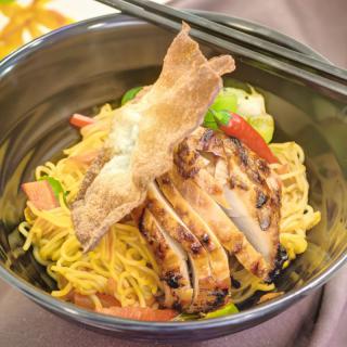 A delicious bowl of noodles topped with grilled chicken, vegetables, and a crispy piece.