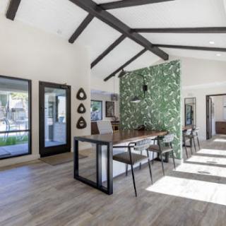A modern dining area featuring a green accent wall and wooden beams, flooded with natural light.