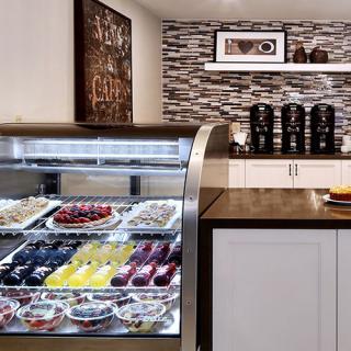A cozy cafe with a dessert display case filled with pastries and a coffee station in the background.