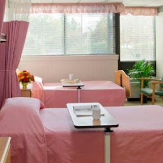 A bright and clean hospital patient room with two beds, each equipped with a bedside table.