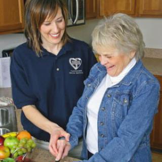 A caregiver assisting an elderly woman in the kitchen.
