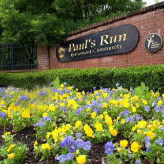 Entrance sign of a community surrounded by vibrant yellow and purple flowers.
