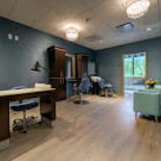 A modern office interior with wooden flooring, featuring a desk, chairs, and elegant lighting.