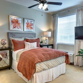 A cozy and well-decorated bedroom featuring warm tones, unique artwork above the bed, and a television by the window.