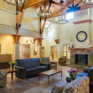 A cozy living room with comfortable seating, chandeliers, and a fireplace, featuring wood beam architecture and natural lighting.