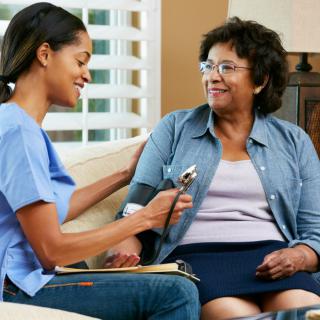 A nurse takes the blood pressure of a patient during a home visit.