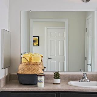 A neatly organized bathroom countertop with a mirror reflecting the door, featuring towels in a basket and small plant decor.