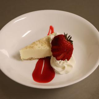 A delightful slice of cheesecake topped with a fresh strawberry, whipped cream, and a drizzle of strawberry sauce.