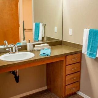A clean and organized bathroom with a sink, mirror, and teal towels.