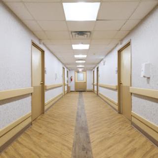 A well-lit hospital hallway featuring doors on either side and a wooden floor.