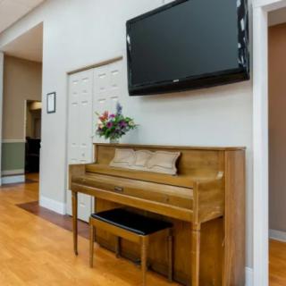 A cozy living room with a wooden piano and a large TV mounted on the wall.
