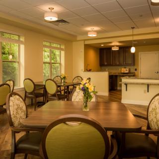 A cozy dining area featuring wooden tables and upholstered chairs, with natural lighting illuminating the space.