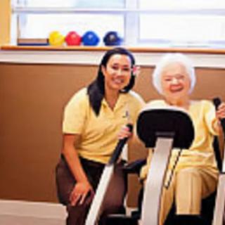 An elderly woman exercising with the assistance of a caregiver in a healthcare facility.