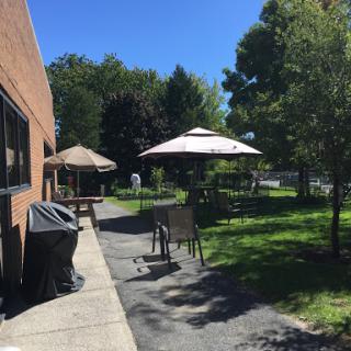 A sunny outdoor area featuring seating and shaded umbrellas, surrounded by greenery.