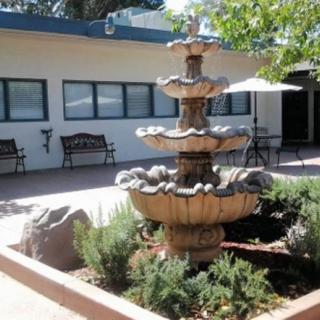 A tiered fountain in a courtyard garden area, surrounded by greenery and a building in the background.
