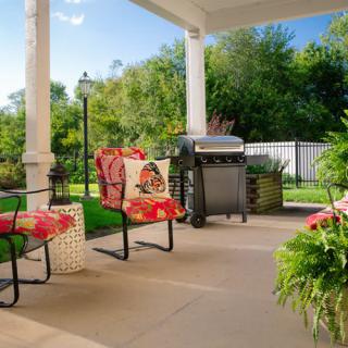 A cozy patio setup with chairs, a grill, and vibrant plants in a garden setting.