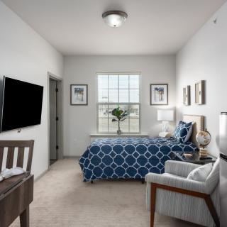 A modern bedroom with blue patterned bedding, a wall-mounted TV, and ample natural light from the window.