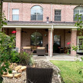 A peaceful backyard patio with comfortable outdoor seating and well-maintained garden in front of a brick house.