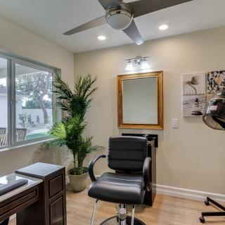 A modern hair salon interior with a chair facing a mirror, complemented by lush plants and ample natural lighting.