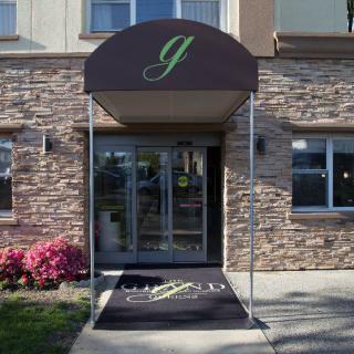 A building entrance featuring a glass door with a brown awning and a welcome mat, surrounded by stone walls and landscaping.