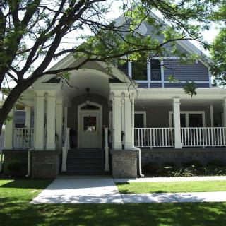 A classic residential house with a spacious front porch and shaded by large trees.