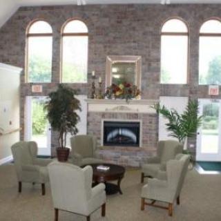 A cozy lounge area featuring a brick wall with a fireplace, surrounded by comfortable chairs and decorative plants.