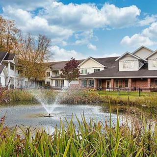 A serene view of houses by a pond with a fountain under a partly cloudy sky.