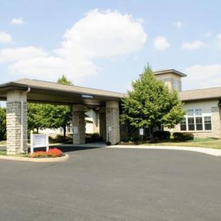 A building with a covered entrance and surrounding trees on a sunny day.