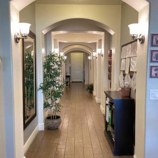 A well-lit hallway featuring arched doorways, decorative plants, and framed artworks along the walls.