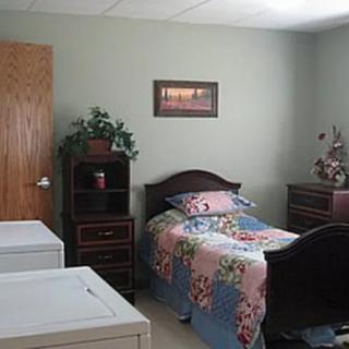A cozy bedroom featuring a single bed with colorful bedding, wooden furniture, and decorative plants.