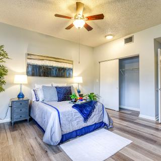A cozy bedroom with stylish decor, featuring a comfortable bed, ceiling fan, and hardwood flooring.