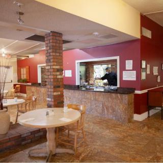 A cozy restaurant interior with tables, chairs, a brick column, and a serving counter against red walls.
