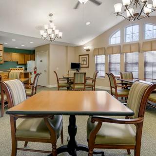 A well-lit dining and seating area with several tables and chairs, featuring a kitchenette in the background.