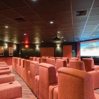An empty theater room with rows of comfortable seating facing a large screen.