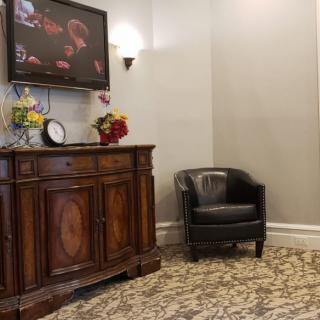 A waiting room with a leather armchair, a decorative cabinet, and a wall-mounted television.