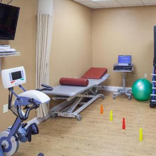 A physical therapy room equipped with a stationary bike, treatment table, exercise ball, and colorful cones for rehabilitation exercises.