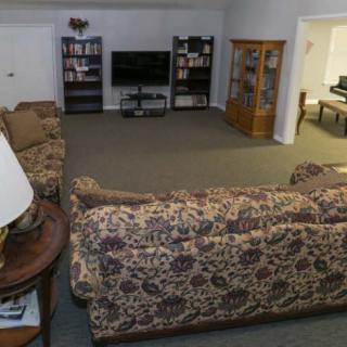A cozy living room with patterned sofas, a television, bookshelves, and carpeted flooring.