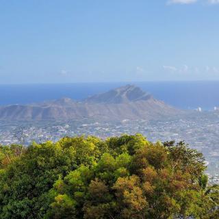 A scenic view of a mountain range with the ocean in the background and lush greenery in the foreground.