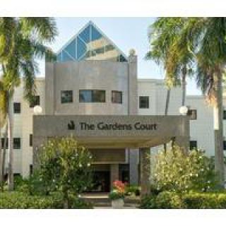 The entrance of The Gardens Court hotel surrounded by palm trees.