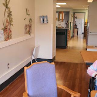 A spacious, well-lit waiting area in a healthcare facility, featuring comfortable seating and a view into the kitchen.