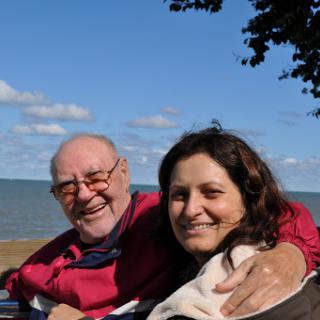 A joyful moment shared between an elderly man and a woman, smiling together with a scenic background.