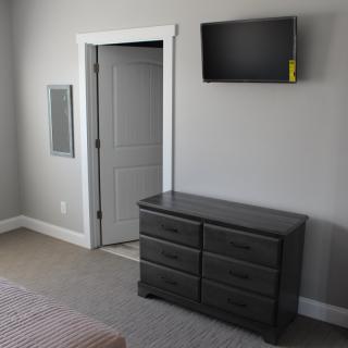 A minimalist bedroom featuring a wall-mounted television and a gray dresser.