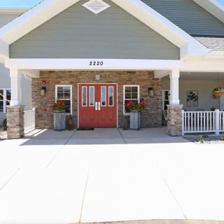 A welcoming building entrance with red double doors, adorned by flowers and supported by stone pillars.