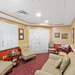 A cozy waiting room with sofas and chairs arranged on a carpeted floor, featuring warm lighting and decor.
