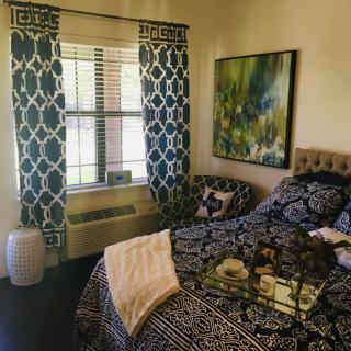 A cozy bedroom interior featuring patterned curtains, a decorated bed, and a large painting on the wall.