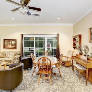 A cozy living room featuring comfortable seating, a wooden dining table, decorative elements, and a large window allowing natural light.