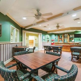 Cozy restaurant interior with wooden tables and chairs, featuring ceiling fans and a bar area.