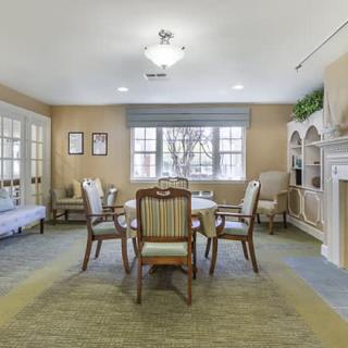 A cozy living space featuring a table with chairs, surrounded by elegant furnishings and natural light from the windows.