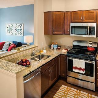 A modern kitchen with stainless steel appliances, wood cabinets, and a granite countertop.